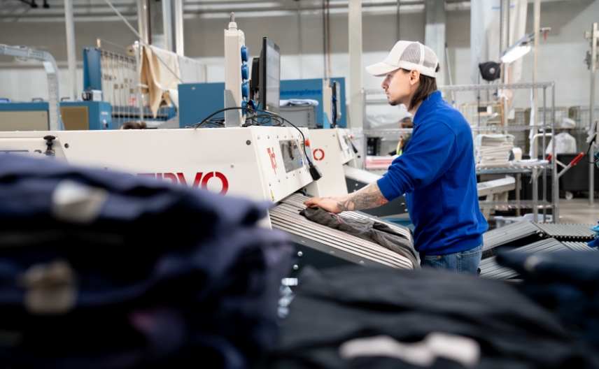 Medewerker behandelt kledingstuk aan de plooimachines in de industriële wasserij.